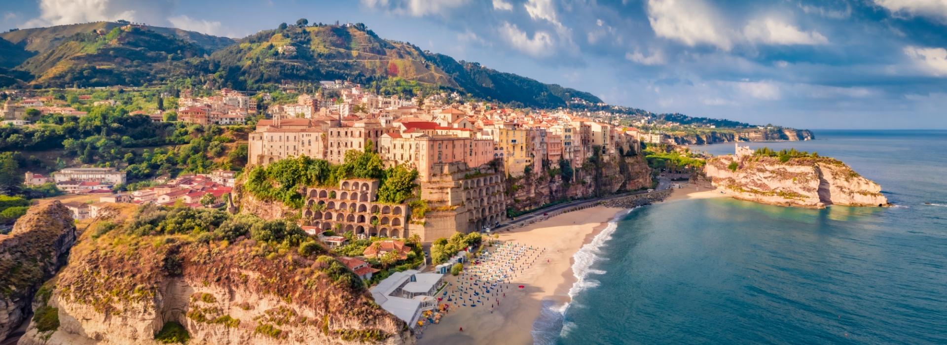 Panorama costiero di una città mediterranea con spiaggia, scogliere e mare cristallino.